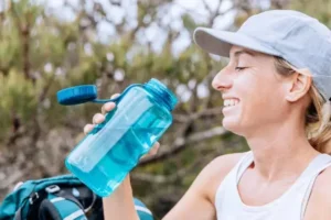 Woman drinking from a 32 oz water bottle during outdoor activity, showing the practical size for daily hydration.